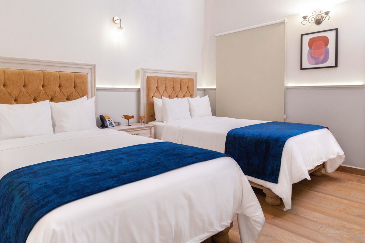 A hotel room with two beds, white bedding, and blue throw blankets.