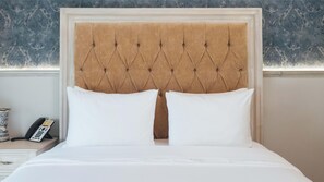 A bed with a tufted headboard, two white pillows, and a bedside table with a telephone. - Voco Royalty Puebla Downtown (Puebla)