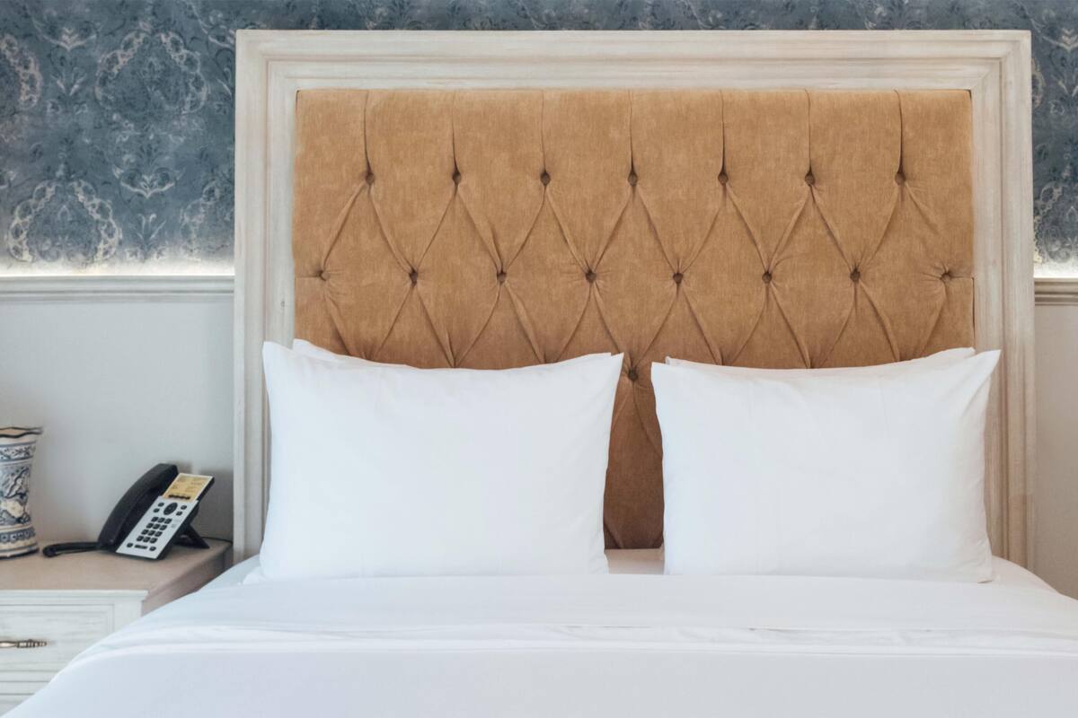 A bed with a tufted headboard, two white pillows, and a bedside table with a telephone.