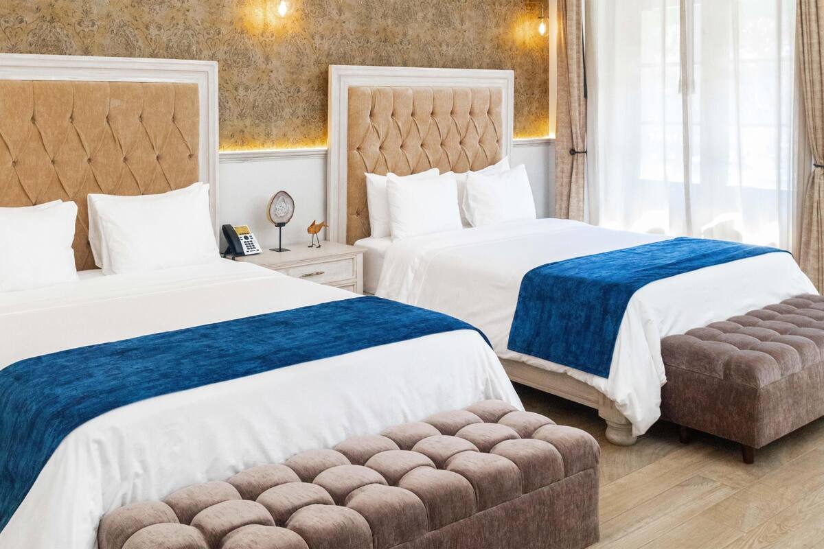 A double bed with a blue accent, a bedside table with a lamp, and a wall-mounted phone.