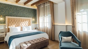 A bedroom with a large bed, a tufted headboard, a bench, a chair, and a nightstand with a lamp. - Voco Royalty Puebla Downtown (Puebla)