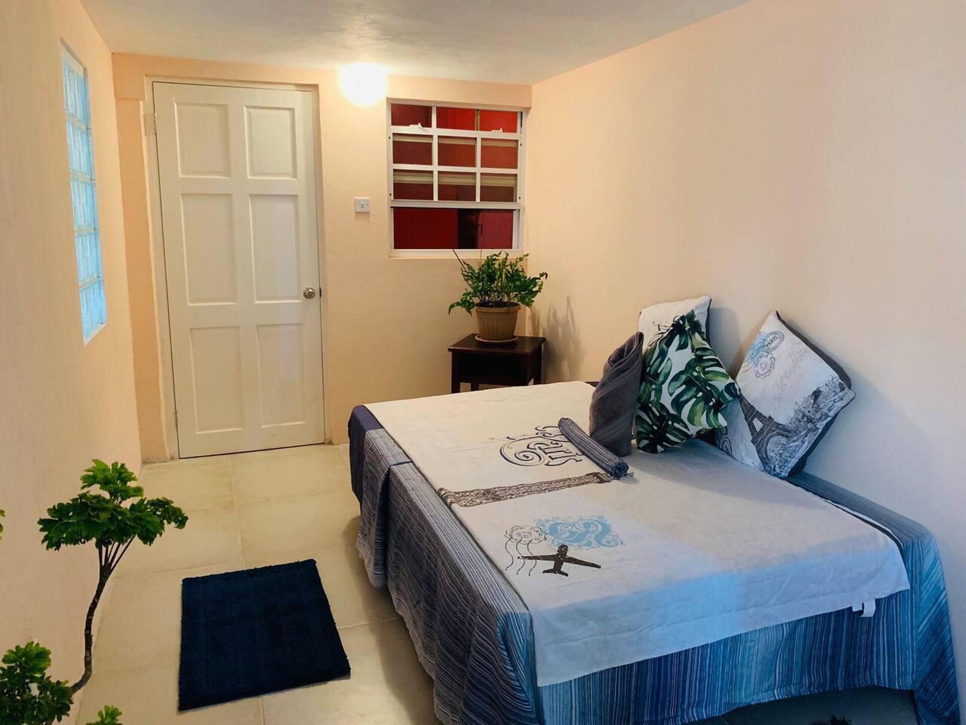 A bedroom with a bed, a potted plant, a window, and a door.
