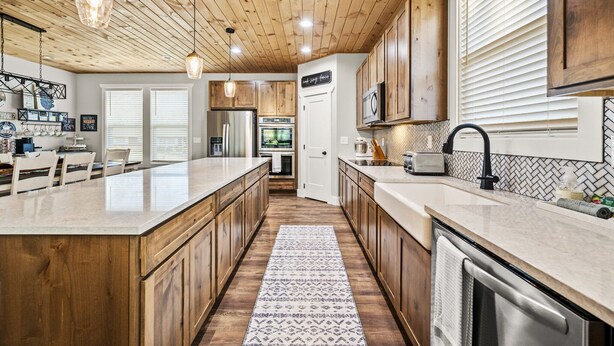 A modern kitchen with wooden cabinets, a large island, stainless steel appliances, and pendant lighting.