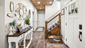 A hallway with a wooden ceiling, white walls, a staircase, and a sign reading "OUR HAPPY PLACE".