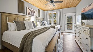 A bedroom with a large bed, a ceiling fan, and a view of the outdoors through a door.