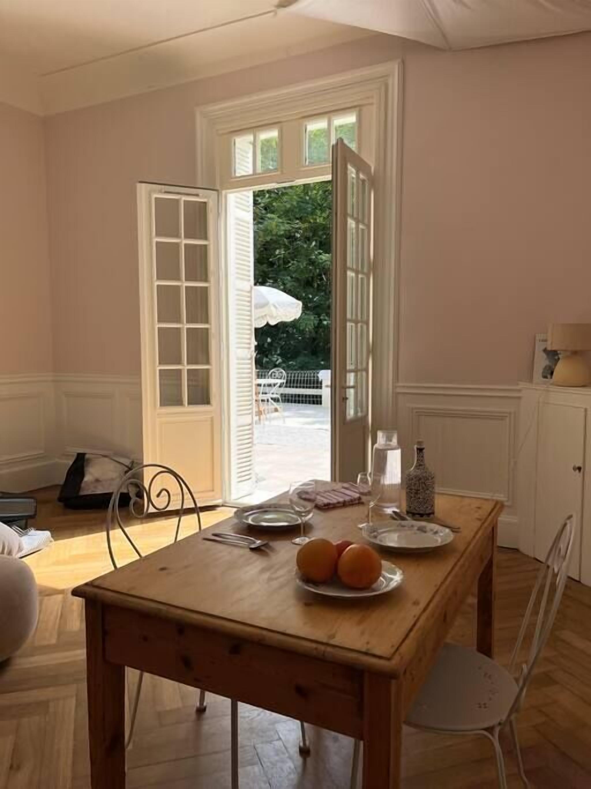 Un espace repas avec une table en bois, des chaises et une vue sur l’extérieur grâce à une porte ouverte.