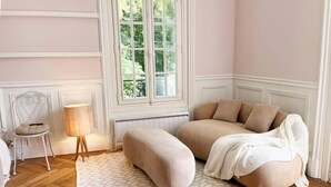 A room with a large window, a sofa, a chair, and a lamp. - Royal Rose (Étretat)
