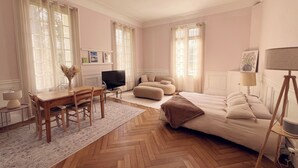 A spacious room with a large bed, a television, a dining area with a table and chairs, and a sofa. - Royal Rose (Étretat)