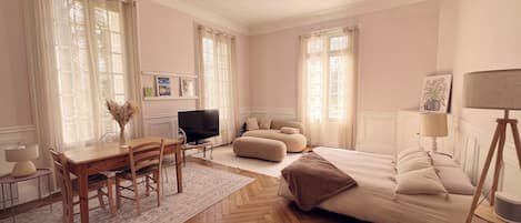 A spacious room with a large bed, a television, a dining area with a table and chairs, and a sofa.