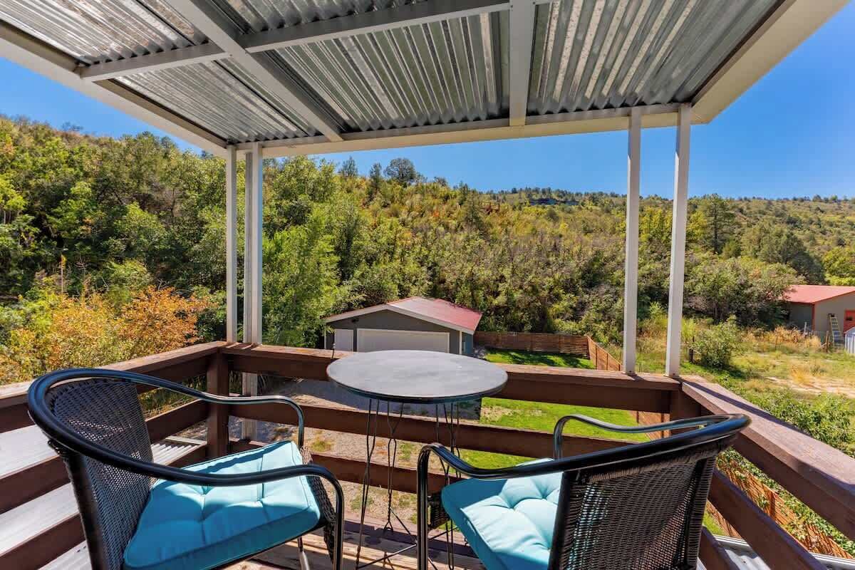 Un espace extérieur abrité, avec une table et des chaises, offrant une vue sur un paysage boisé.