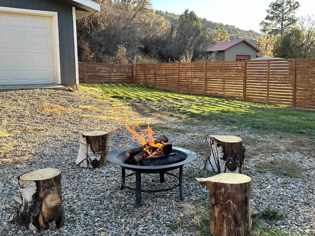 A backyard with a fire pit, wooden stools, and a gravel area.