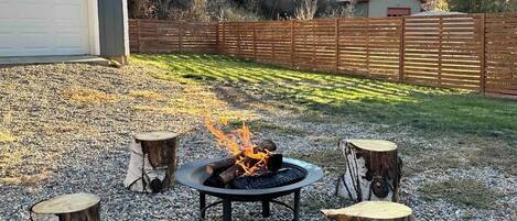 A backyard with a fire pit, wooden stools, and a gravel area.