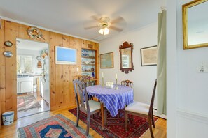 Un comedor con pared de paneles de madera, ventilador de techo, mesa con mantel azul y sillas.