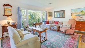 A cozy living room with a large window, a wooden table, and a patterned rug.