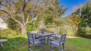 A patio with a table and chairs, surrounded by greenery and trees.