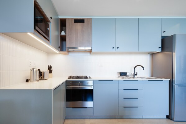 A modern kitchen with stainless steel appliances, light blue cabinetry, and a white countertop.