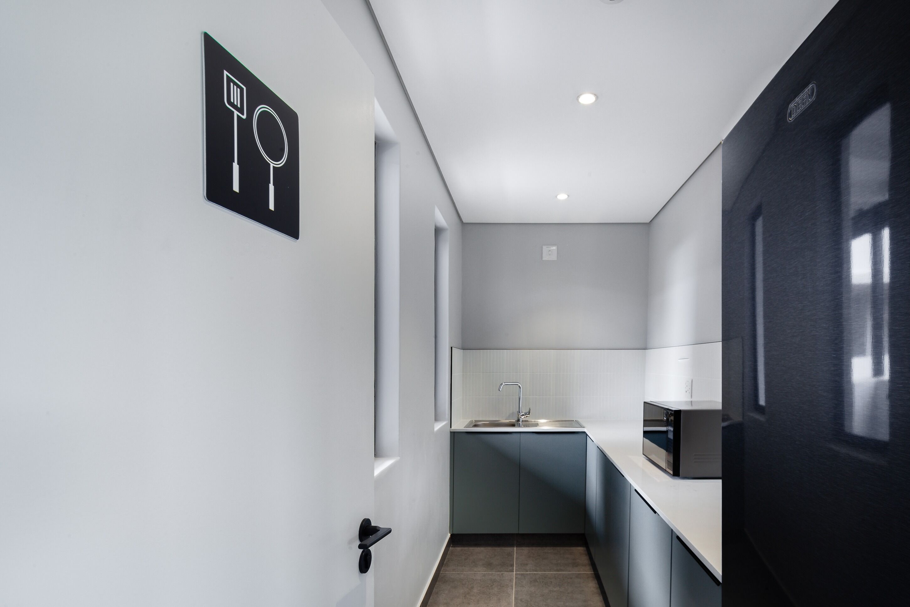 A modern kitchen with a microwave, sink, and a blackboard with utensils.