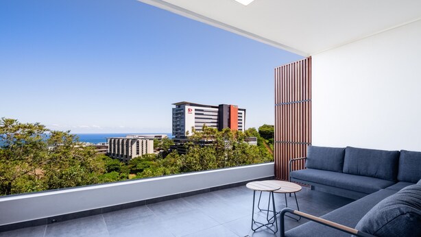 Un balcón moderno con un sofá, una mesita y vistas a la ciudad y al océano.