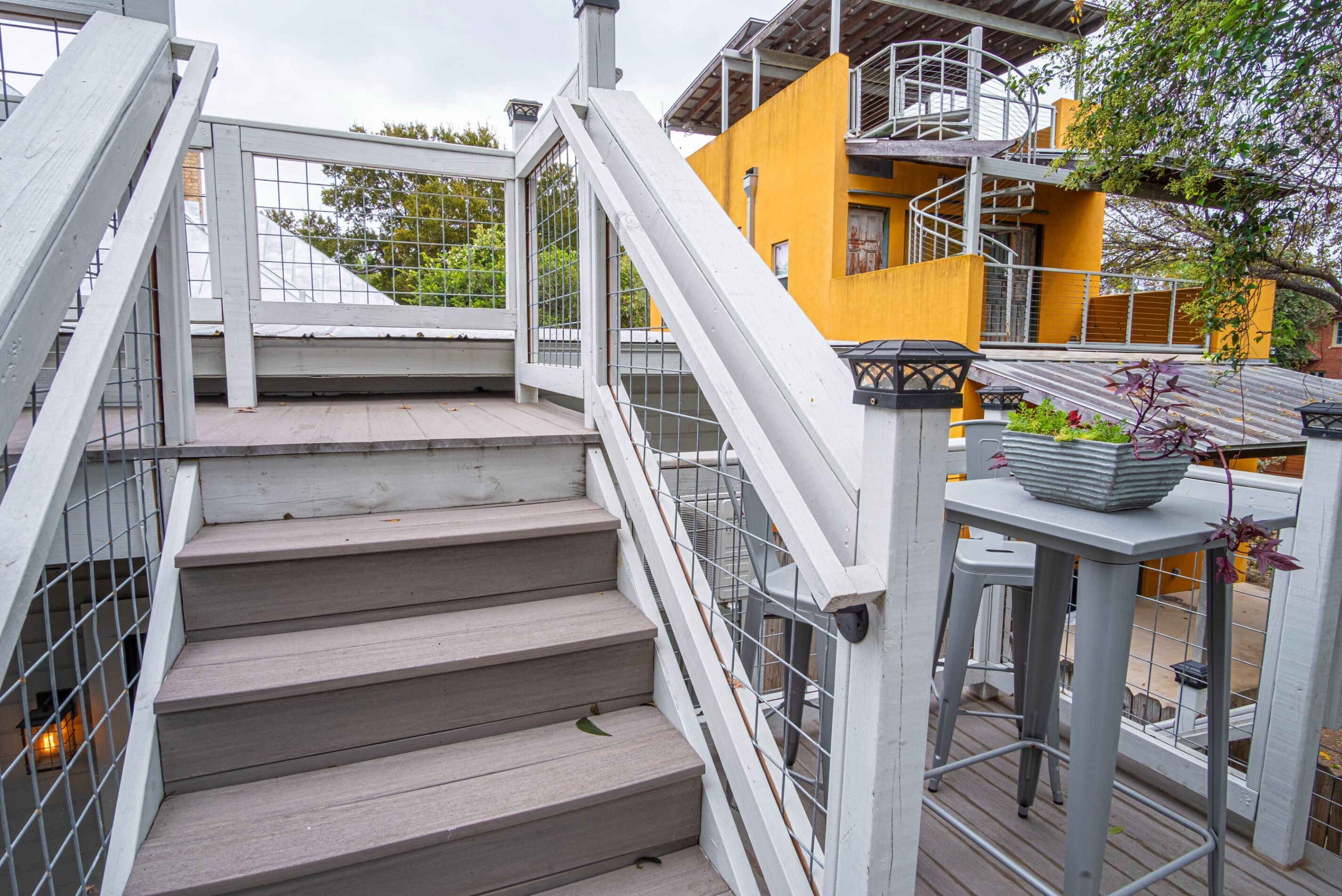 Un conjunto de escaleras exteriores de madera con barandillas de metal que conducen a un edificio amarillo con una escalera de caracol.