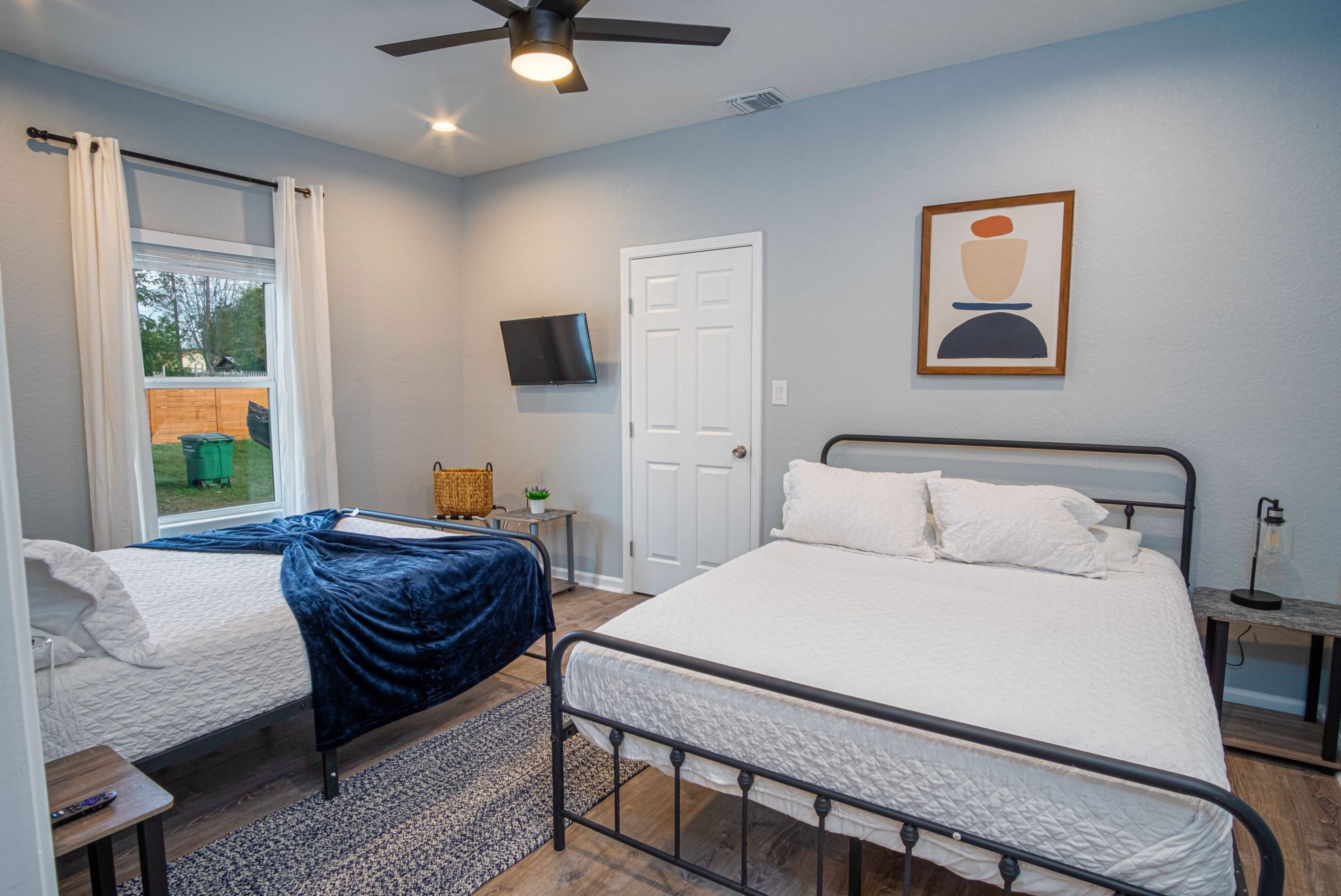 A bedroom with two beds, a ceiling fan, a TV mounted on the wall, and a door.