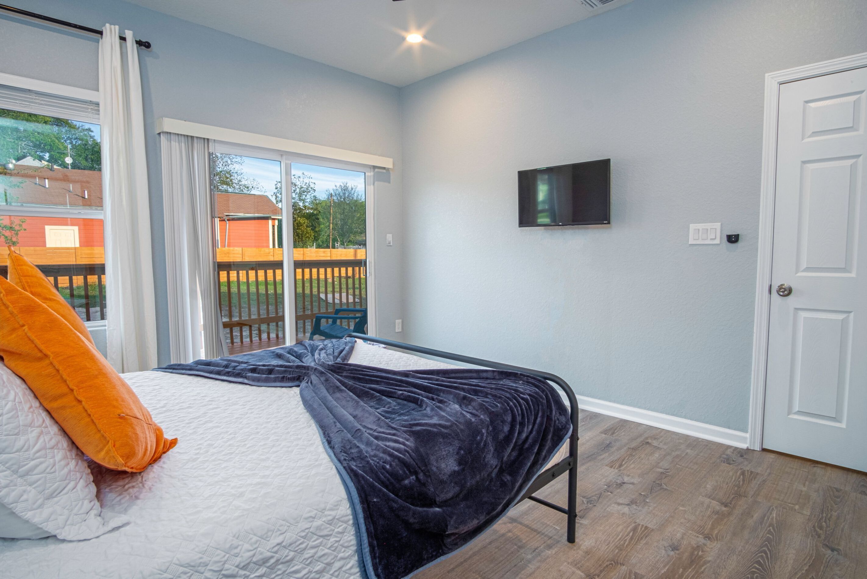 A bedroom with a bed, a TV mounted on the wall, and a sliding glass door leading to an outdoor area.