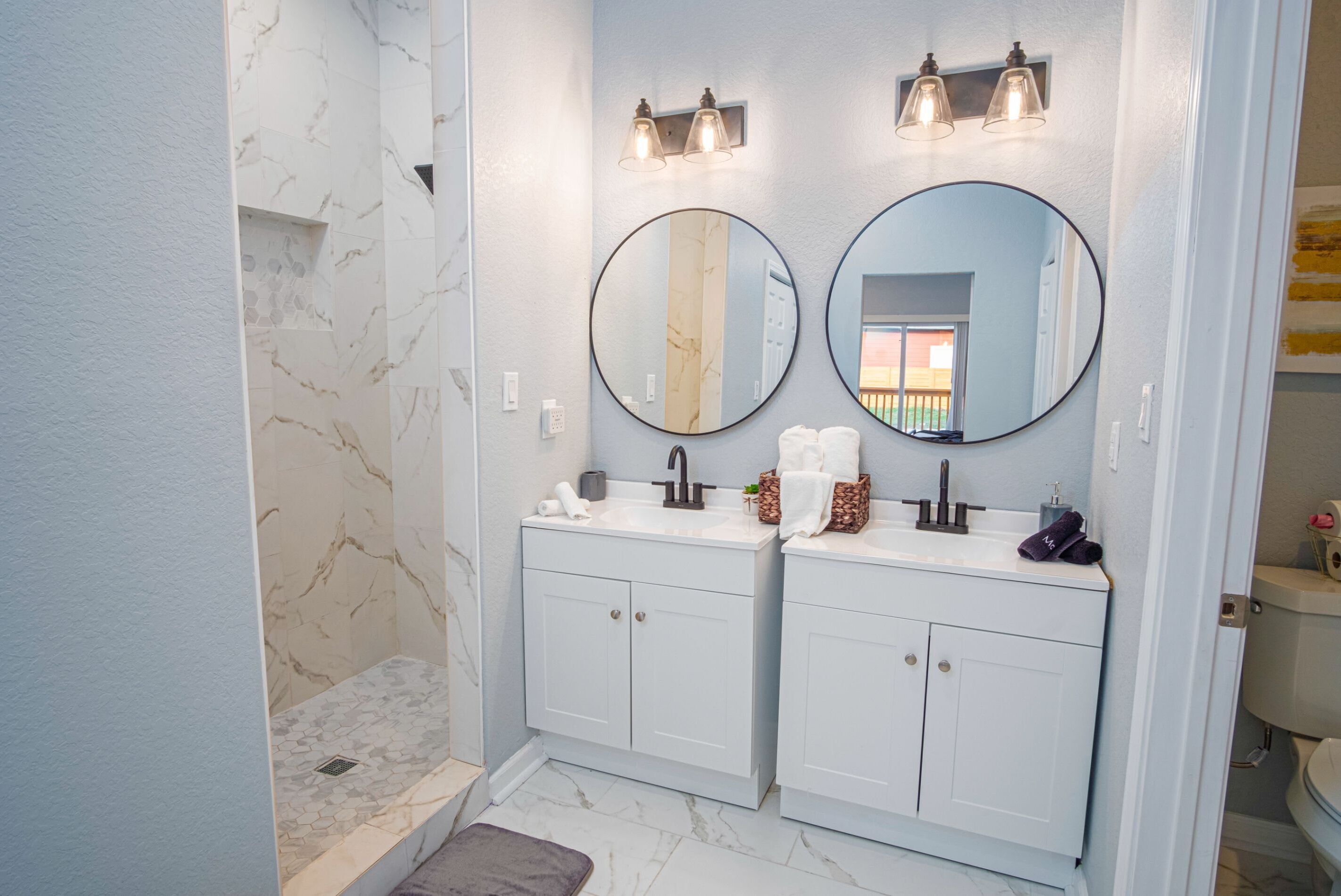 A bathroom with two sinks, a shower, and two wall-mounted mirrors.
