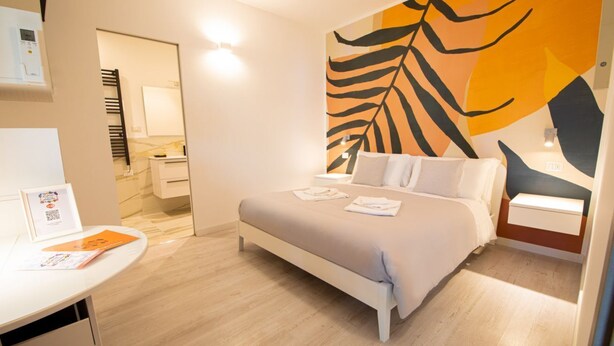 Habitació d'hotel moderna amb un llit gran, una taula de treball i una paret amb un dibuix de fulles.