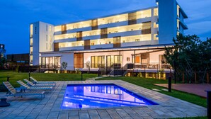 Un hôtel moderne doté d’une piscine, d’un espace extérieur aménagé et d’une façade bien éclairée.