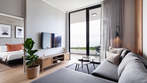 Un salon moderne avec un canapé, une table basse, un téléviseur et une grande fenêtre avec des rideaux.