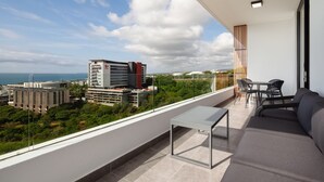 Un balcon aménagé avec un canapé, une table et des chaises, offrant une vue sur le paysage urbain, avec ses bâtiments et sa verdure.