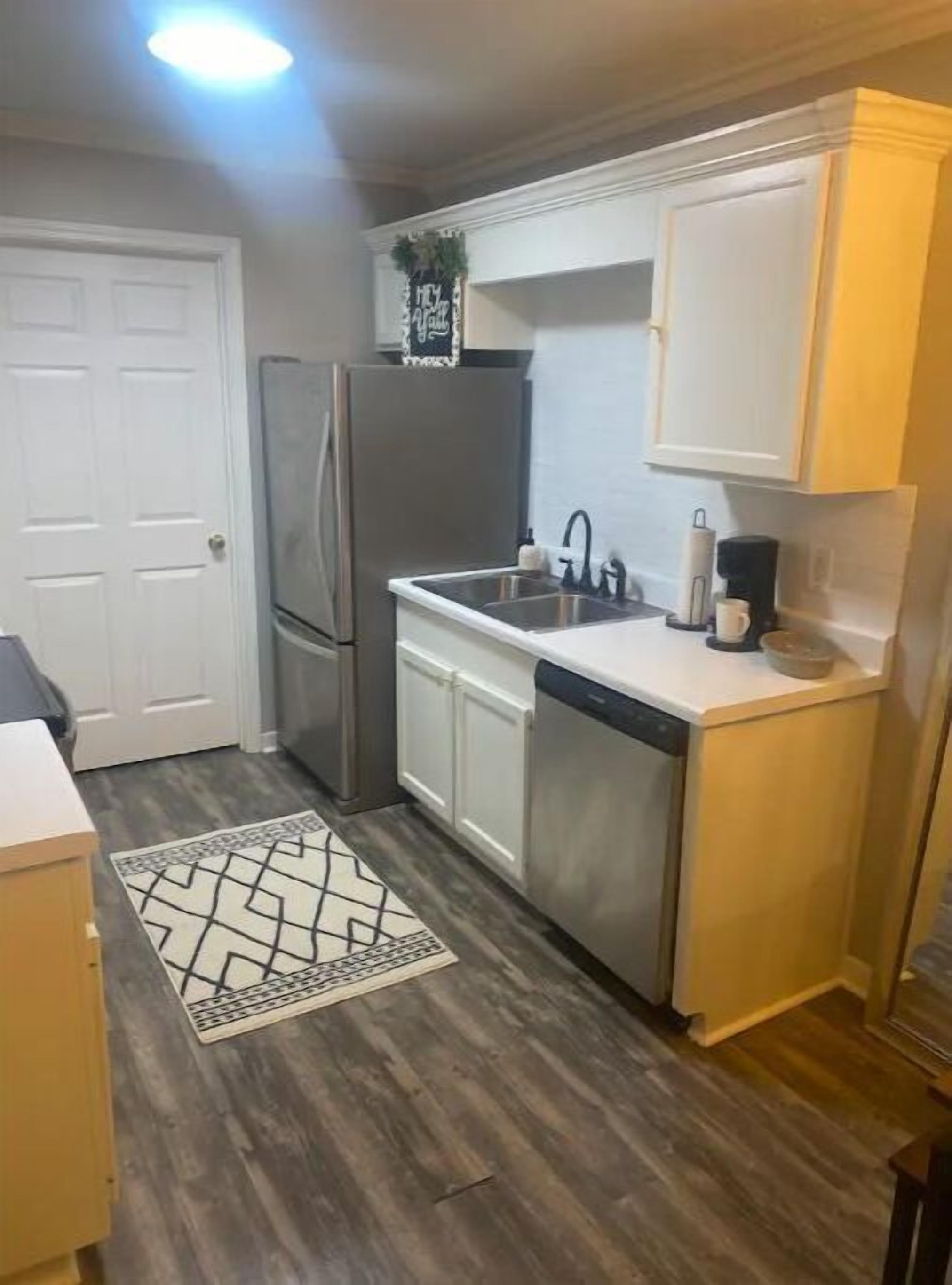 A compact kitchen with a refrigerator, sink, and dishwasher, a patterned rug, and a door.