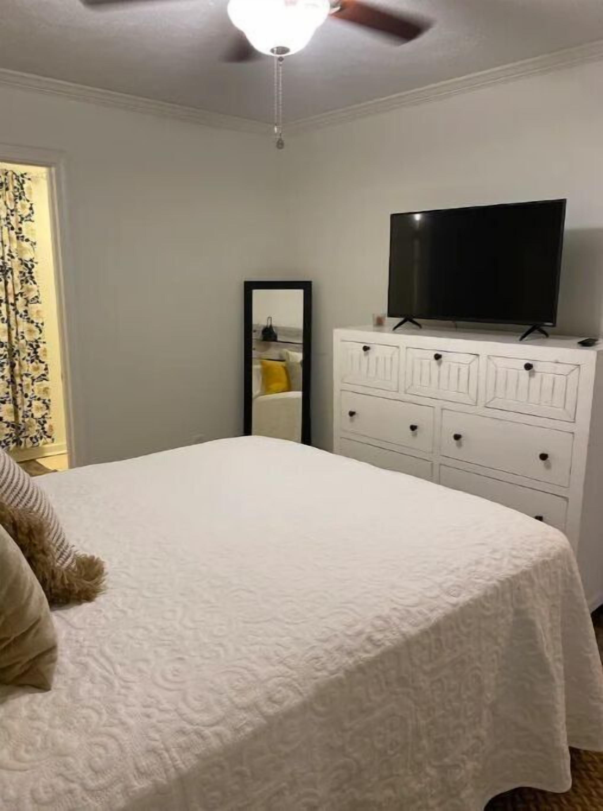 A bedroom with a bed, a dresser, a television, and a ceiling fan.