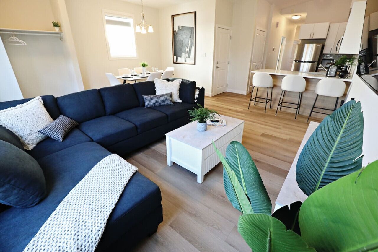 A modern living room with a dark blue sectional sofa, a white coffee table, and a large green plant.