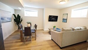 Ein modernes Wohnzimmer mit einem beigen Sofa, einem Esstisch mit Stühlen und einer großen Kühlpflanze.