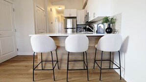 A modern kitchen with white cabinets, a stainless steel range hood, and three white bar stools.