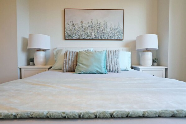 Une chambre à coucher bien aménagée, avec un grand lit, deux tables de chevet dotées de lampes et un tableau accroché au mur.