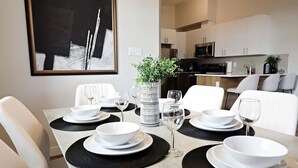 A dining area with a table set for four, including white plates, bowls, and wine glasses. There is a decorative vase with greenery on the table.