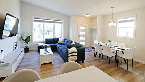 A modern living room with a blue sectional sofa, a dining table set for six, and a TV mounted on the wall.