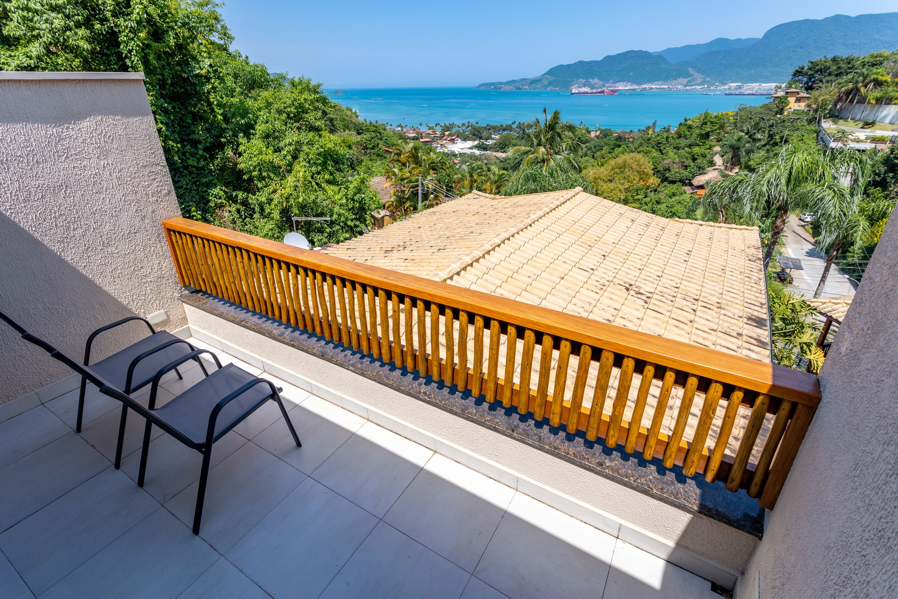 A balcony with a tiled floor, a wooden railing, and two chairs.