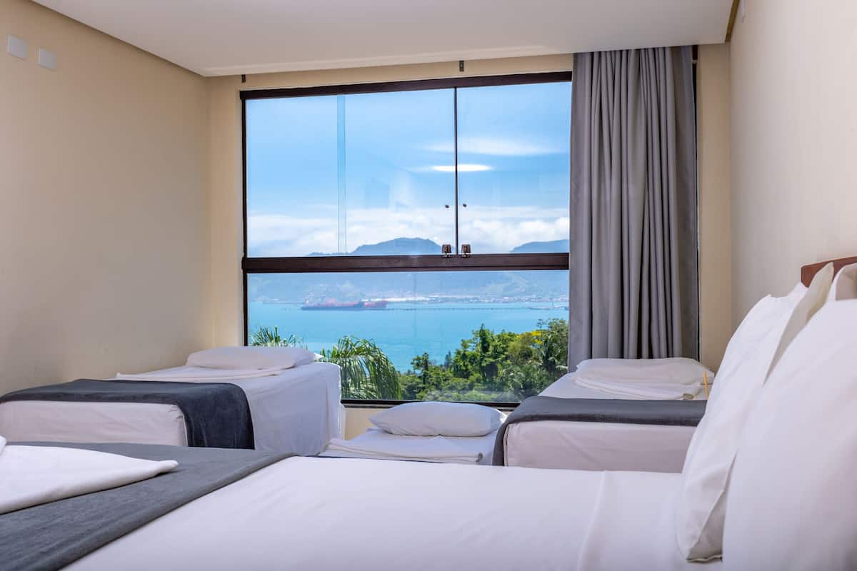 A hotel room with two beds, a large window with a view of the sea and mountains, and a curtain on the window.