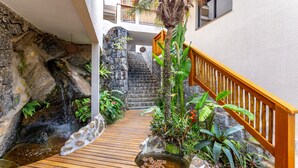 A wooden staircase leading to a balcony with a stone wall and a small waterfall. - Eco Baepi Residence (Ilhabela)