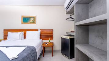 A hotel room with a bed, a small table with a remote control, a TV, and a wall-mounted air conditioner.