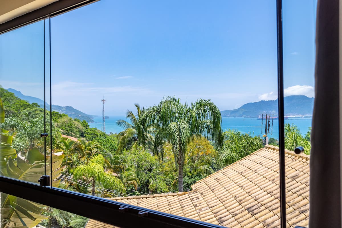 A view from a window overlooking a coastal landscape with palm trees and a tiled roof.