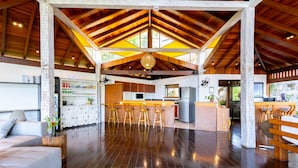 A spacious living area with a high ceiling, wooden beams, and a central bar area with stools. - Eco Baepi Residence (Ilhabela)