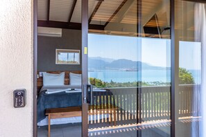 Une chambre à coucher avec un lit, une table de chevet, une fenêtre et une vue sur la mer et les montagnes.