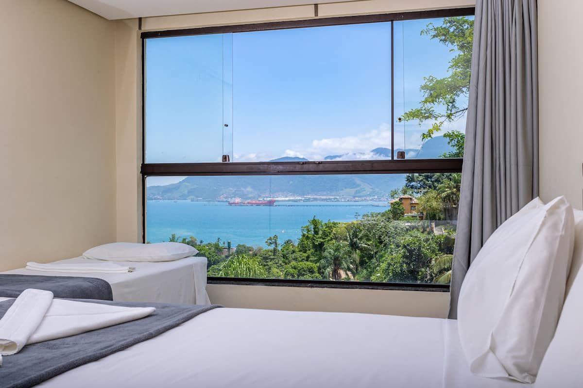 A hotel room with a large window offering a view of the sea and mountains.