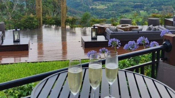 Una mesa redonda con tres copas de vino blanco, un marco de madera y vistas a un paisaje montañoso.