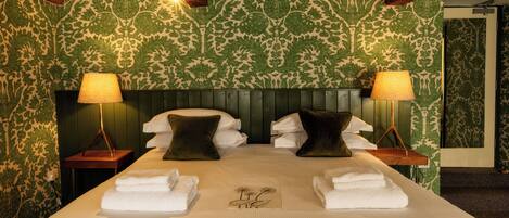 A neatly made bed with white linens, two dark pillows, and two bedside lamps.