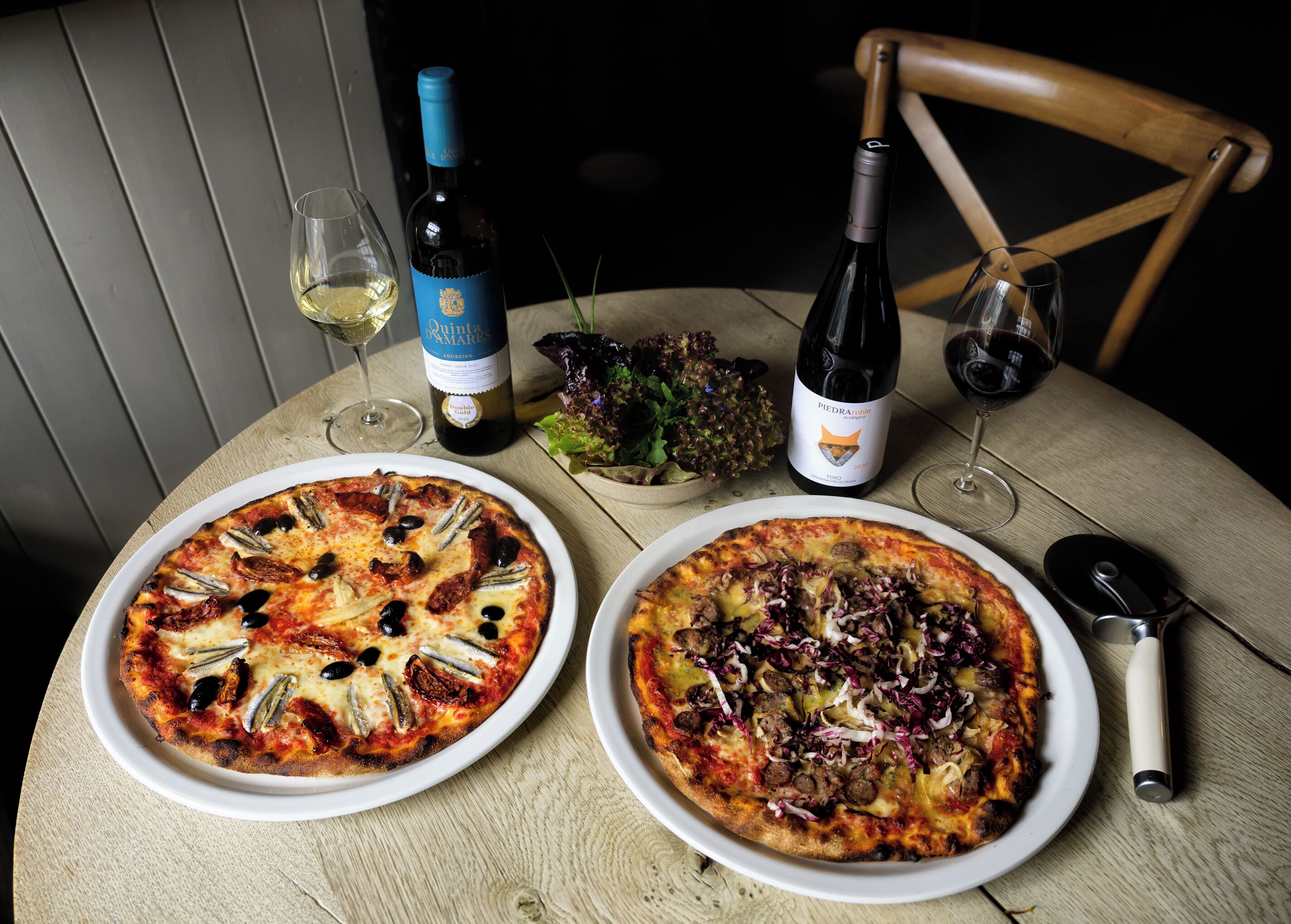 Deux pizzas sur des assiettes, une bouteille de vin et un verre à vin sur une table.