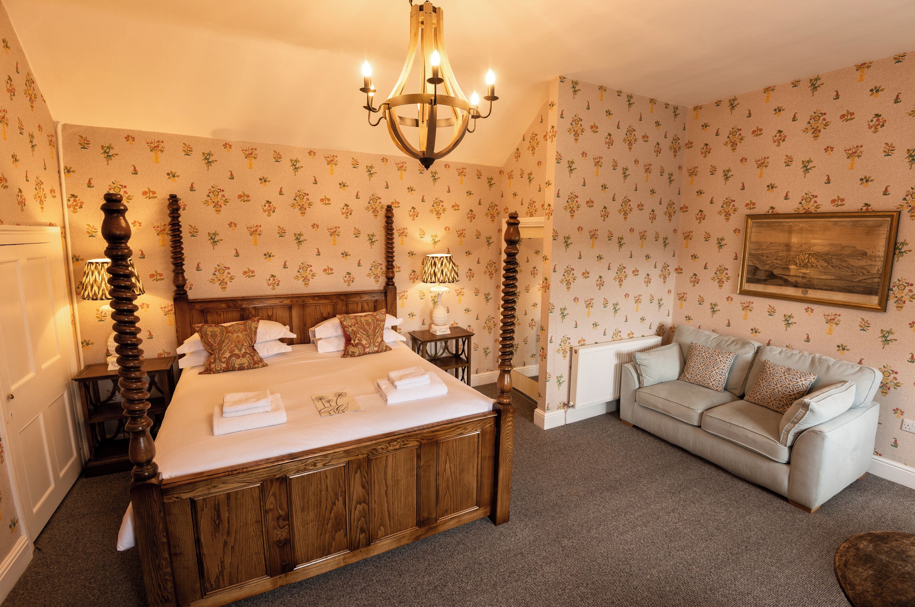 A bedroom with a four-poster bed, a sofa, a chandelier, and floral wallpaper.
